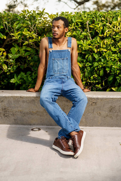 Handsome African American man posing in overalls at a park scene - Fotó, kép