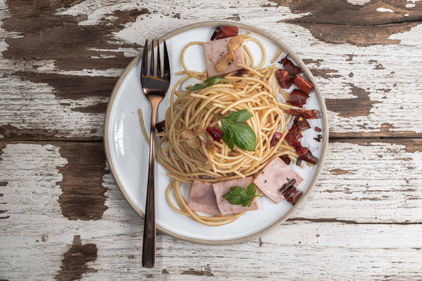 Pasta spaghetti garlic ham dried chili in white plate isolated on wood background close up, top view, food concept. - 写真・画像