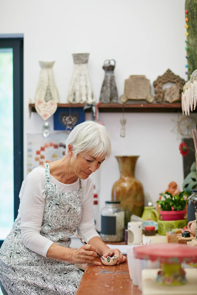 Её собственный уголок. Снимок пожилой женщины, делающей керамический горшок в мастерской. - Фото, изображение