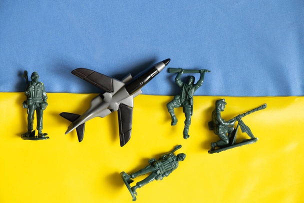 Ένα παιδικό παιχνίδι αεροπλάνο και στρατιώτες βρίσκονται στις εθνικές σημαίες της Ουκρανίας, ο πόλεμος στην Ουκρανία, οι στρατιωτικές δυνάμεις στη χώρα 2022 - Φωτογραφία, εικόνα