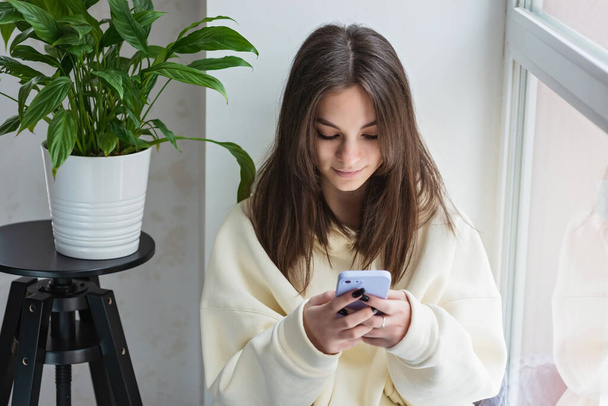Happy teenage girl looking at smartphone, relaxing at home, enjoy using mobile online apps, playing games on mobile phone, checking messages or social media messages. Soft selective focus. - Photo, Image