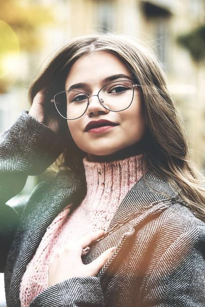 Retrato de moda de una hermosa joven de 16-20 años, vestida con un suéter de punto rosa, gafas y una gabardina clásica gris. - Foto, Imagen