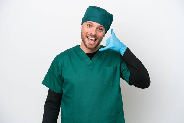 Surgeon Brazilian man in green uniform isolated on white background making phone gesture. Call me back sign - Фото, изображение