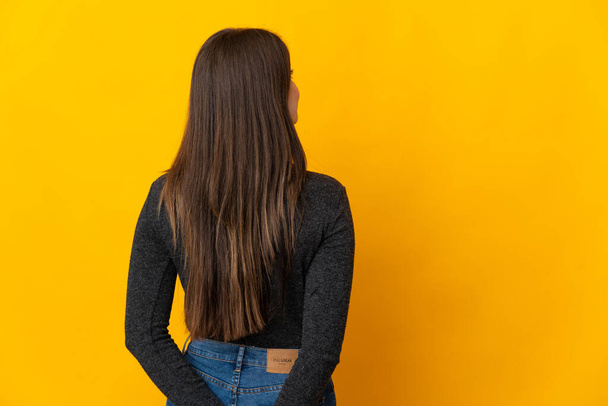 Adolescente brasileña aislada sobre fondo amarillo en posición de espalda y mirando hacia atrás - Foto, imagen