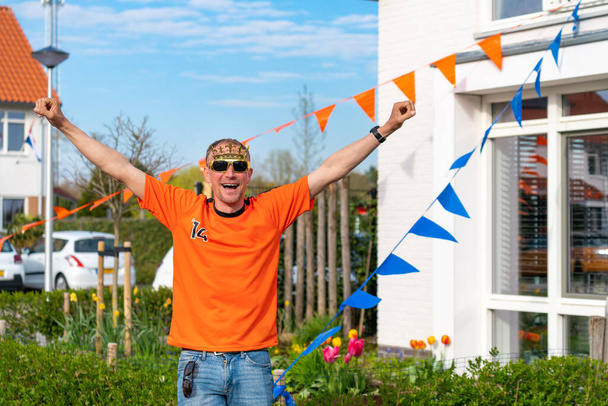 Dutchman celebrating kings day on the road during a street party dressed in orange in Holland the Netherlands. Koningsdag is a traditional festival to celebrate the Dutch royal family. Dutch flag and bunting decorating the houses. - Valokuva, kuva