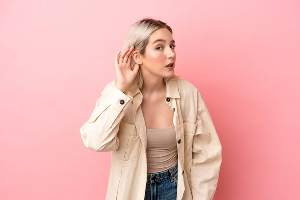 Young caucasian woman isolated on pink background listening to something by putting hand on the ear - Фото, зображення