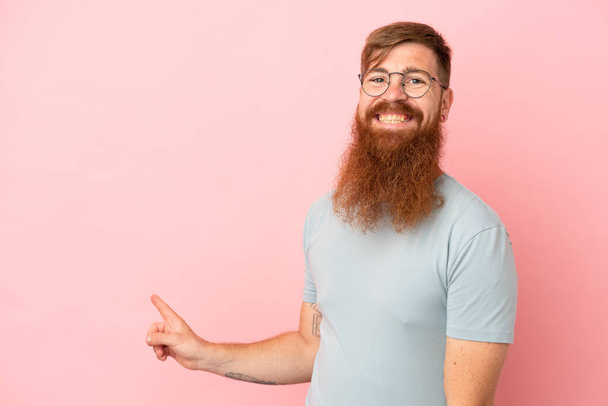 Young reddish caucasian man isolated on pink background pointing finger to the side and presenting a product - Photo, Image