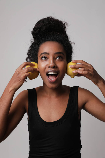 Vertical portrait of young woman posing with three parts of lemon on white wall. - Фото, зображення