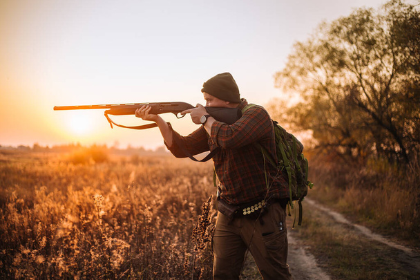 Joven soldado fuerte con rifa y cinturón de municiones que se mueve al aire libre por el camino de tierra en el tiempo de puesta del sol - Foto, imagen