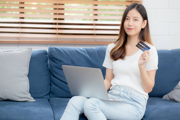 Молода азіатка сидить на дивані, використовуючи покупки ноутбуків онлайн з кредитною карткою, купуючи в Інтернеті, щаслива дівчина платить з електронним бізнесом на дивані, покупка та оплата, бізнес-концепція
. - Фото, зображення
