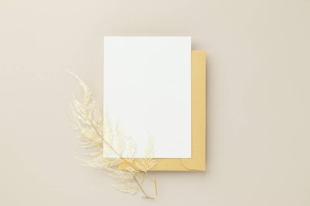 ブランクグリーティングカード招待状mockup 5x7オンブラウン封筒で乾燥した花でベージュ背景,フラットレイ, mokup - 写真・画像