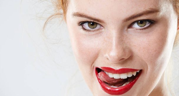 Syčí jako čert. Closeup studio portrét krásné mladé ženy na sobě červené rtěnky kousání její jazyk. - Fotografie, Obrázek