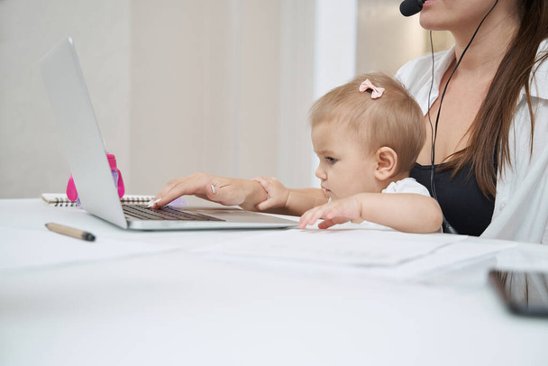 Baby grabbing mother hand while she typing on laptop keyboard - Foto, afbeelding