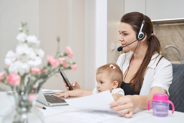 Mother with baby calling on smartphone while working at laptop - Foto, Bild