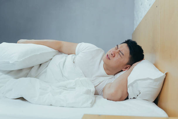Sad Asian lying in a bed under a blanket, a depressed man in the morning - Φωτογραφία, εικόνα
