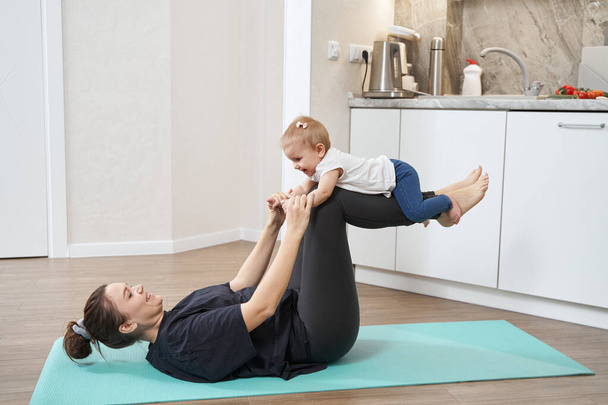 Mother working out on sport mat with her child - Фото, зображення