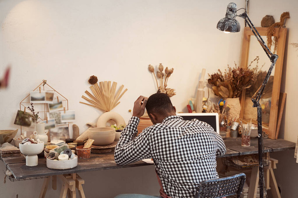 African American potter scrutinizing documentation in workplace - Фото, зображення