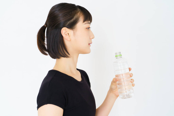 Asiática joven mujer hidratante en ropa deportiva en interiores - Foto, Imagen