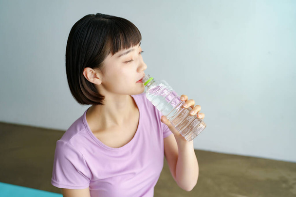 Asiatico giovane donna idratante in sportswear indoor - Foto, immagini