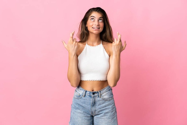 Young caucasian woman isolated on pink background with fingers crossing and wishing the best - Photo, Image