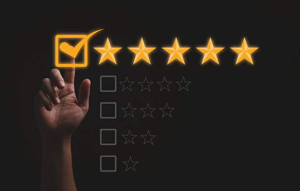 Toucher à la main et marquer cinq étoiles jaunes sur fond noir, la meilleure satisfaction du client et l'évaluation pour un produit et un service de bonne qualité. - Photo, image