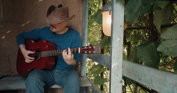 Gitarlı bir adam verandada oturur ve telefonundan mesaj okurken şarkı söyler. - Fotoğraf, Görsel