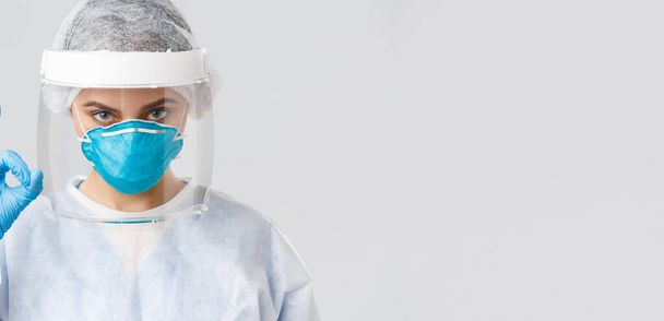 Covid-19, preventing virus, health, healthcare workers and quarantine concept. Close-up of female doctor or nurse in personal protective equipment, rubber gloves, show okay, ensure or guarantee - 写真・画像