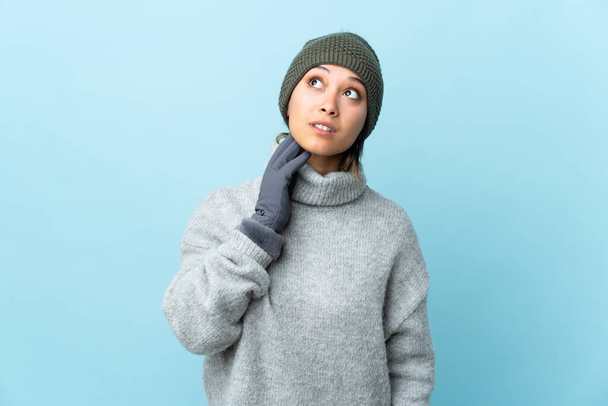 Young Uruguayan girl with winter hat isolated on blue background thinking an idea - Photo, Image