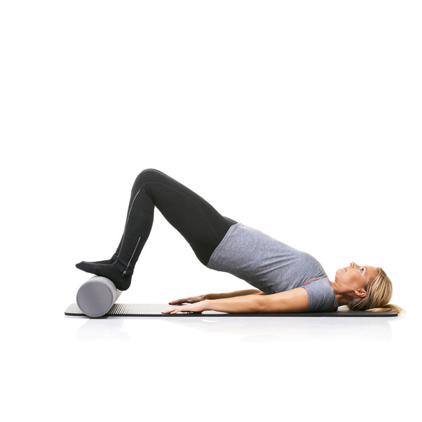 Arching her back. A young woman lying on an exercise mat and using a foam roller to arch her back. - Фото, изображение