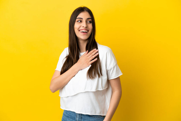 Young caucasian woman isolated on yellow background looking up while smiling - Foto, afbeelding