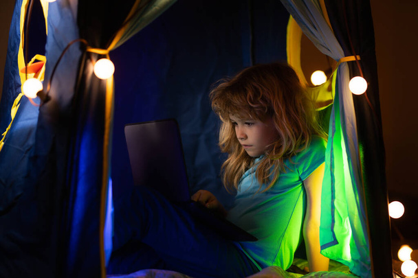 Little kid using laptop by night, child boy illuminated by the blue light of a computer screen. - Photo, image