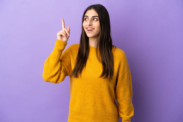 Молода біла жінка ізольована на фіолетовому фоні, збираючись зрозуміти рішення, піднімаючи палець вгору
 - Фото, зображення