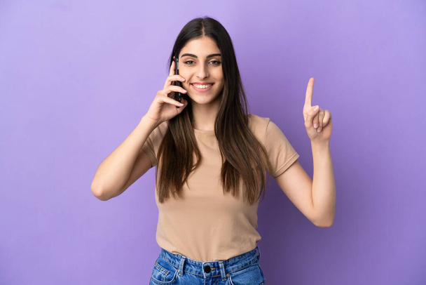 Young caucasian woman using mobile phone isolated on purple background pointing up a great idea - Fotó, kép