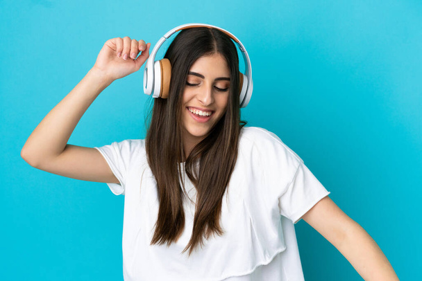 Young caucasian woman isolated on blue background listening music and dancing - Photo, image