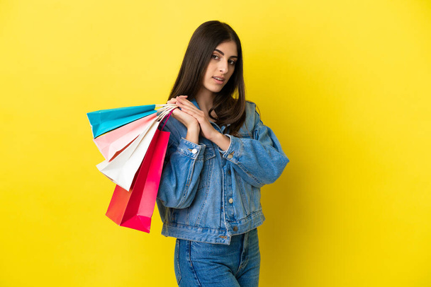 Junge kaukasische Frau isoliert auf blauem Hintergrund mit Einkaufstaschen - Foto, Bild