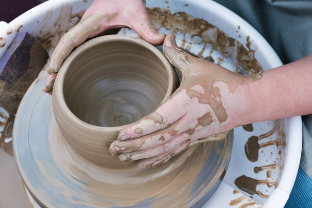 Chiudi le mani lavorando sulla ruota della ceramica e facendo una pentola di argilla, messa a fuoco selettiva - Foto, immagini