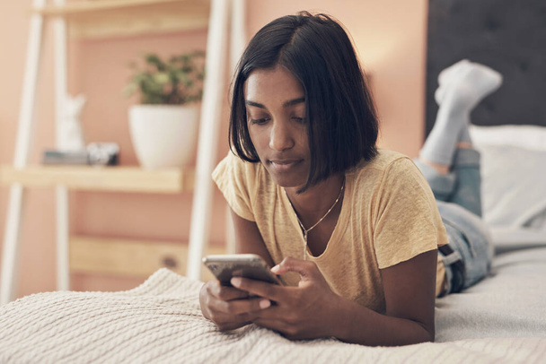 Jaká by byla karanténa bez vašeho společenského spojení. Snímek mladé ženy pomocí smartphonu při relaxaci na posteli doma. - Fotografie, Obrázek
