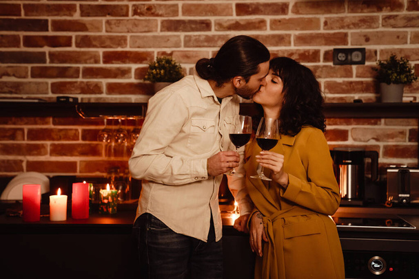 wit romantisch paar zoenen terwijl het drinken van wijn thuis binnen - Foto, afbeelding