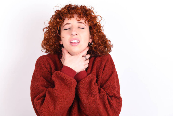 young caucasian woman red haired wearing red sweater over white background keeps shouting suffocate because painful strangle. Health problem. Asphyxiate and suicide concept. - 写真・画像