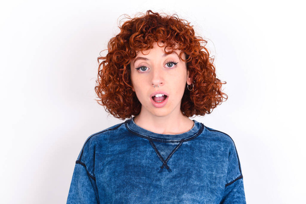Shocked young caucasian woman red haired wearing blue T-shirt over white background stares bugged eyes keeps mouth opened has surprised expression. Omg concept - Fotografie, Obrázek