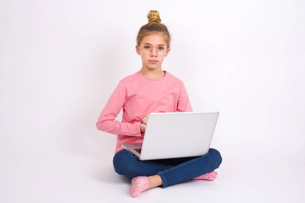 Photo of cheerful confident Beautiful caucasian teen girl sitting with laptop in lotus position on white background arms together - Фото, изображение