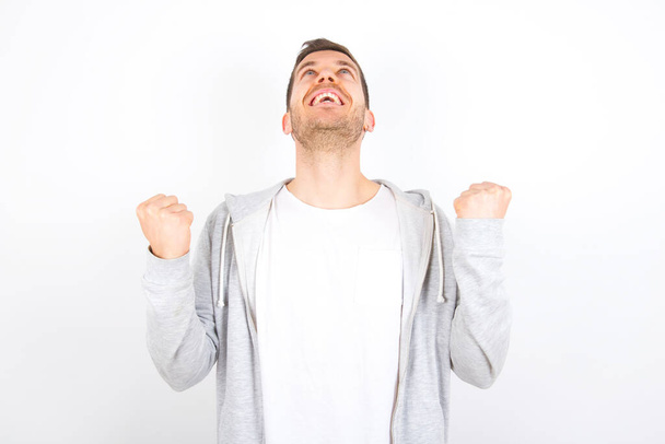 young caucasian man wearing casual clothes over white background looks with excitement up, keeps hands raised, notices something unexpected. - Photo, Image