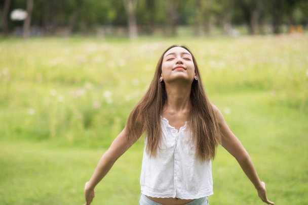 Joven hermosa mujer asiática respirar aire fresco en el campo de flores del parque de primavera. Ella de pie y estirando los brazos con sensación de relax. - Foto, imagen