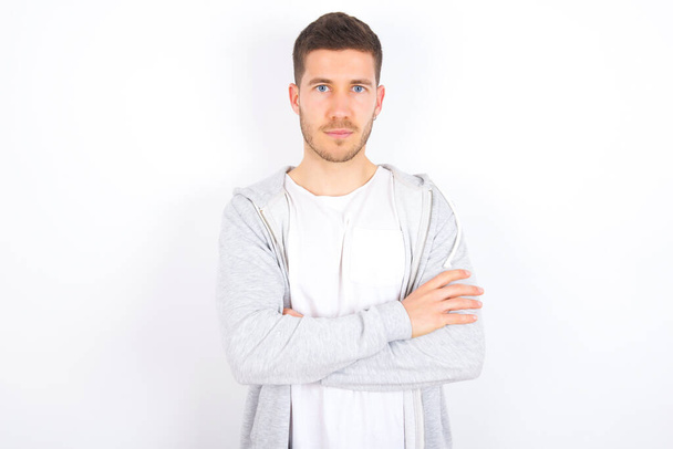 Self confident serious calm young caucasian man wearing casual clothes over white background stands with arms folded. Shows professional vibe stands in assertive pose. - Photo, Image