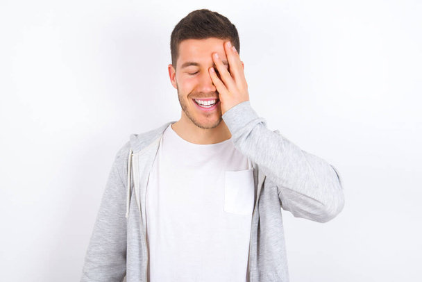 young caucasian man wearing casual clothes over white background makes face palm and smiles broadly, giggles positively hears funny joke poses - Φωτογραφία, εικόνα