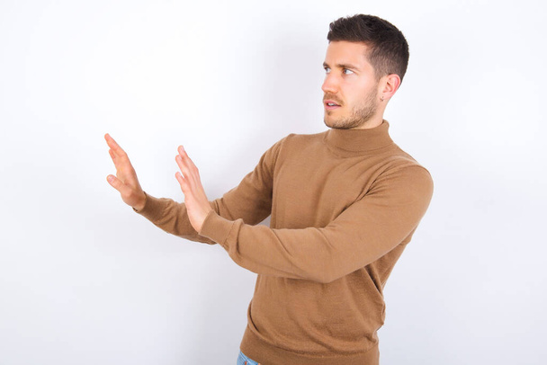 Ontevreden jonge blanke man houdt handen in de richting van lege ruimte en vraagt niet dichterbij te komen ziet iets onplezierigs - Foto, afbeelding