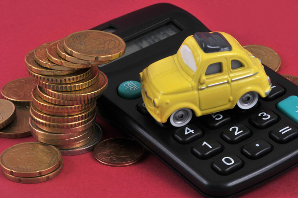 Έννοια του προϋπολογισμού για τις μεταφορές με ένα αυτοκινητάκι σε έναν υπολογιστή με κέρματα ευρώ σε κόκκινο φόντο  - Φωτογραφία, εικόνα