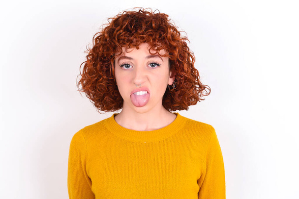 Body language. Disgusted stressed out young redhead girl wearing yellow sweater over white background  , frowning face, demonstrating aversion to something. - Zdjęcie, obraz