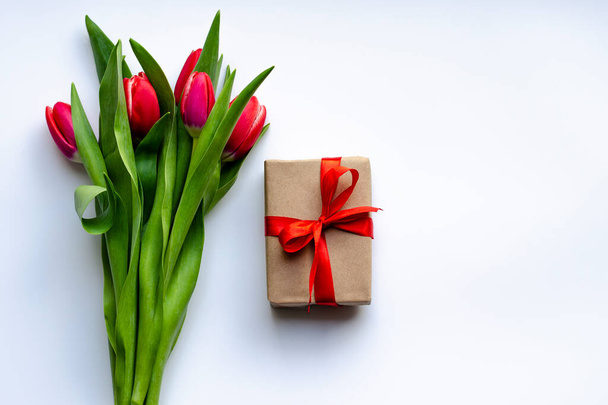 A bouquet of tulips and a gift with a red satin ribbon on a white background. Holiday card - Photo, Image
