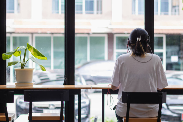 Μια νεαρή γυναίκα κάθεται και ακούει μουσική ενώ εργάζεται στο Διαδίκτυο με το laptop της ευτυχώς μόνη στην καφετέρια. Καλή έννοια εργασίας ακούγοντας μουσική ενώ εργάζεστε - Φωτογραφία, εικόνα